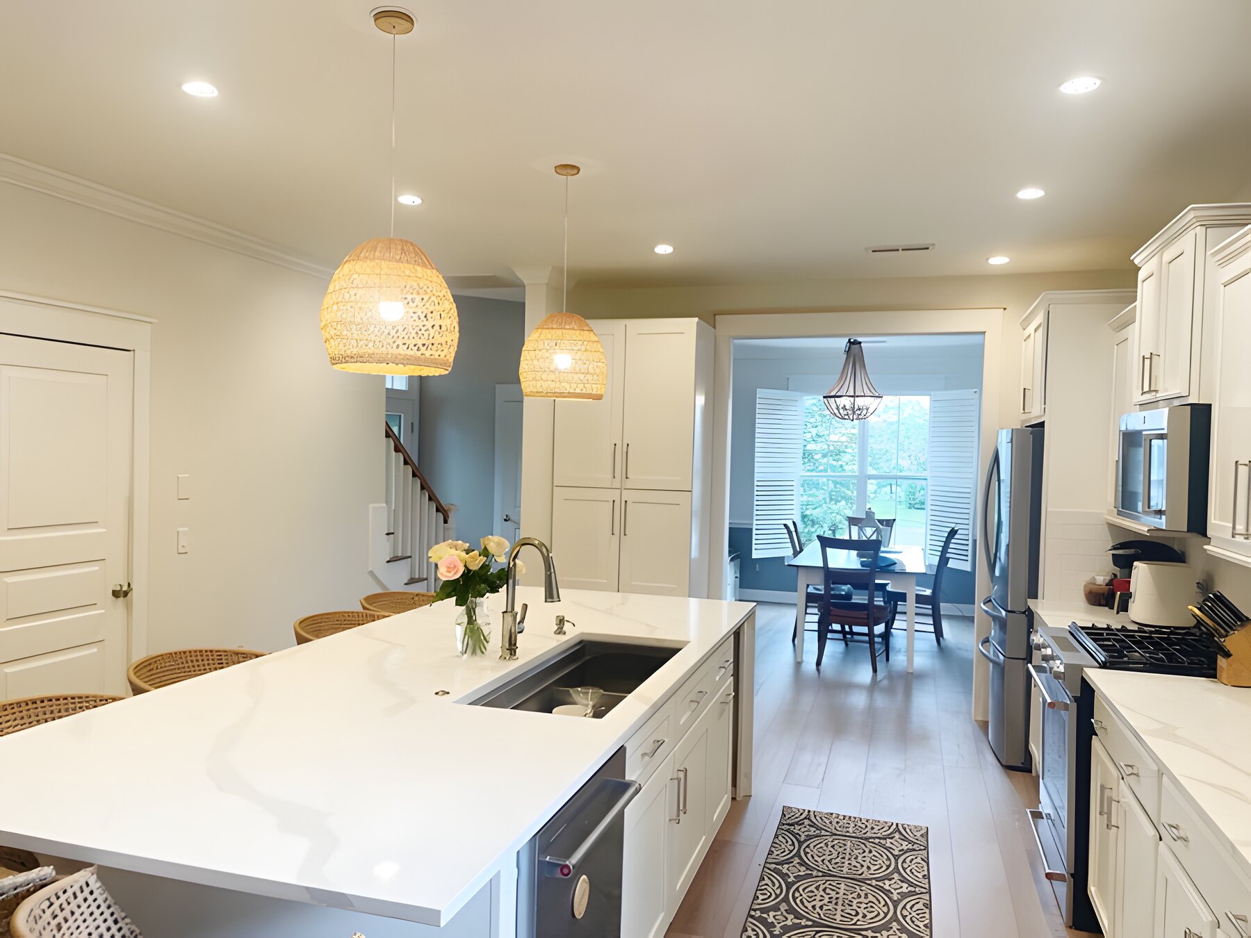 Kitchen after remodel: bright white cabinets, large quartz island with rattan pendants